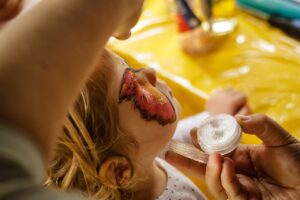 A child getting their face painted and sprinkled with glitter.